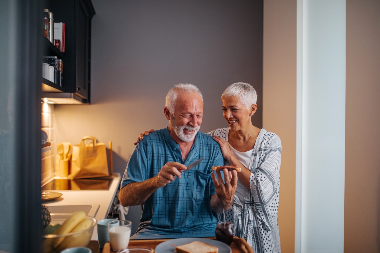 A senior couple laughing while making breakfast in a sunlit kitchen