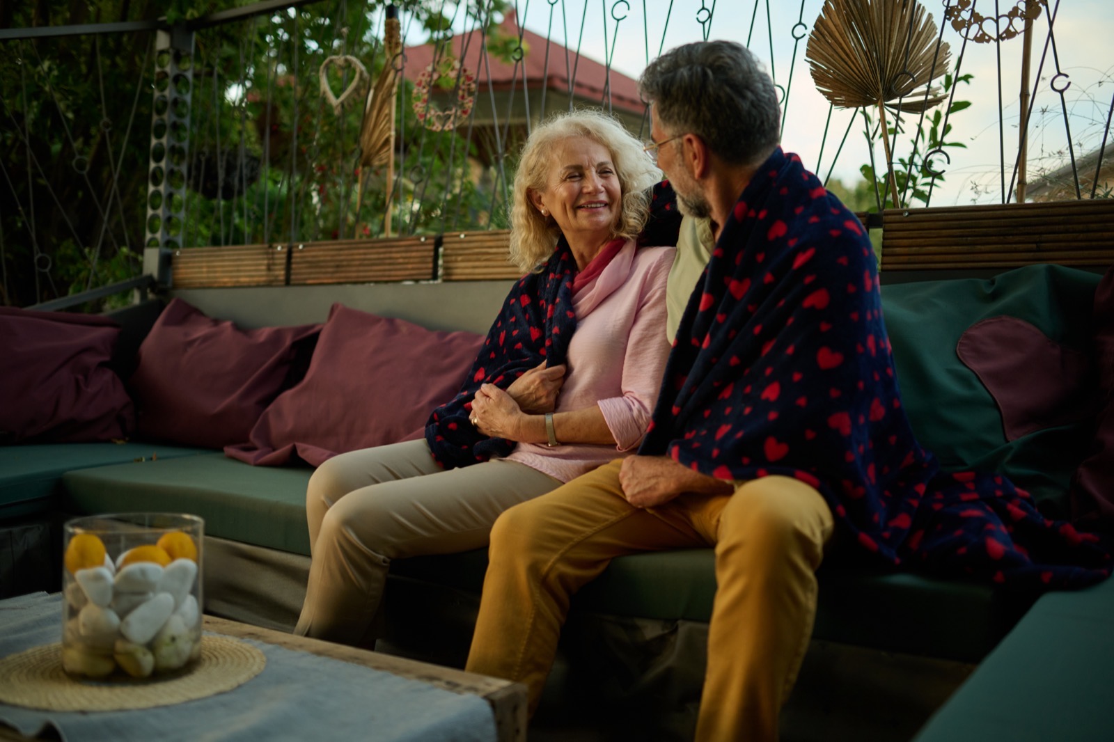 A senior couple wrapped in a blanket on a garden terrace at the end of the season